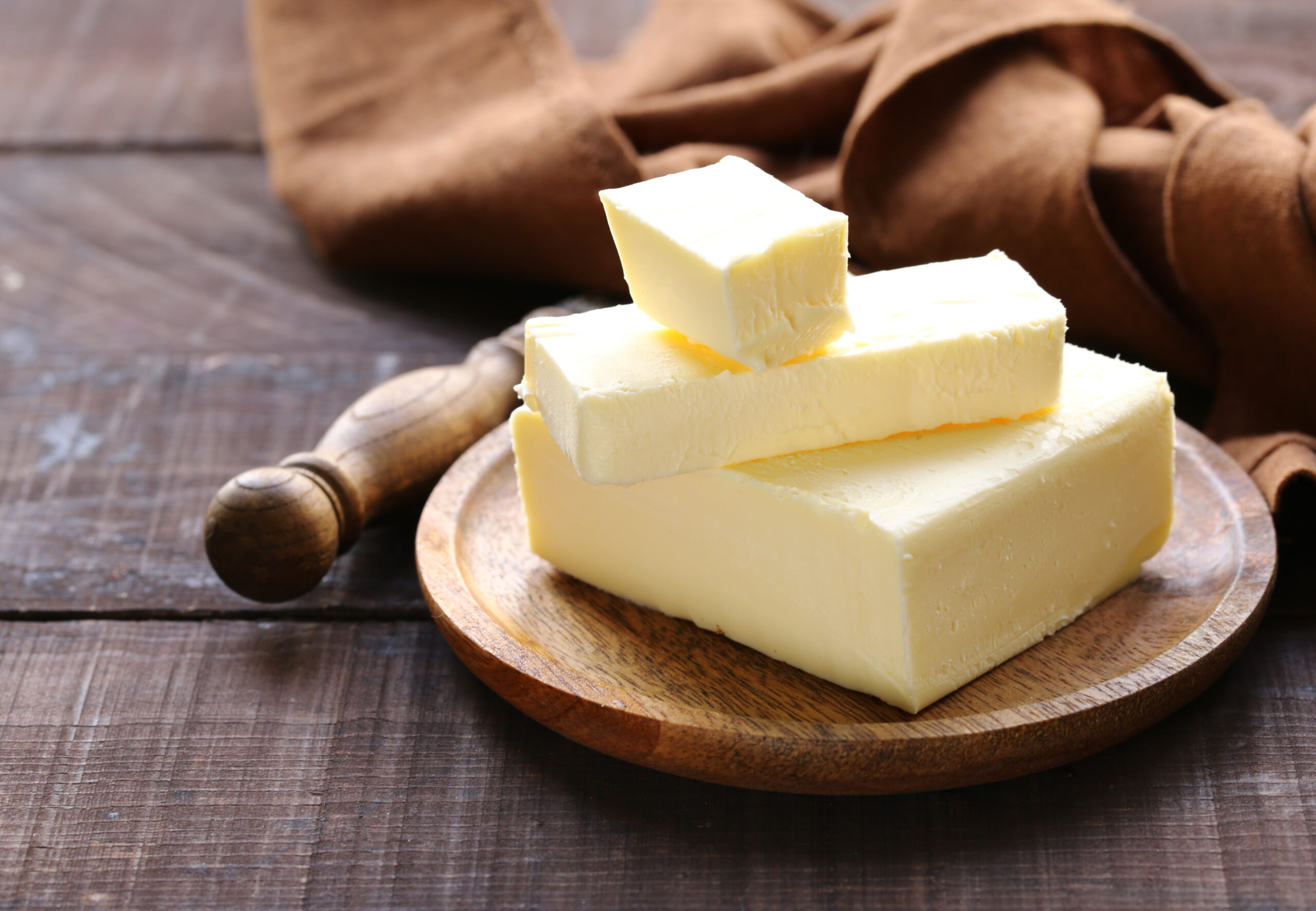 Fresh butter blocks stacked on a wooden plate, with a rustic brown cloth in the background, perfect for cooking and baking.
